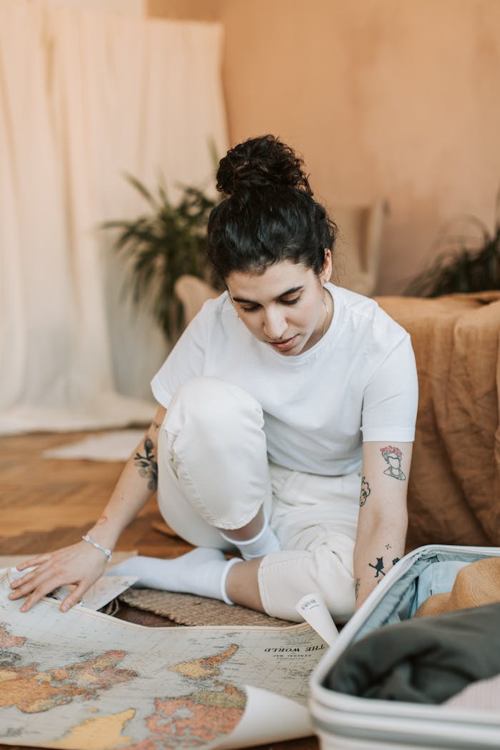 Woman sitting indoors, preparing for travel with map and suitcase.